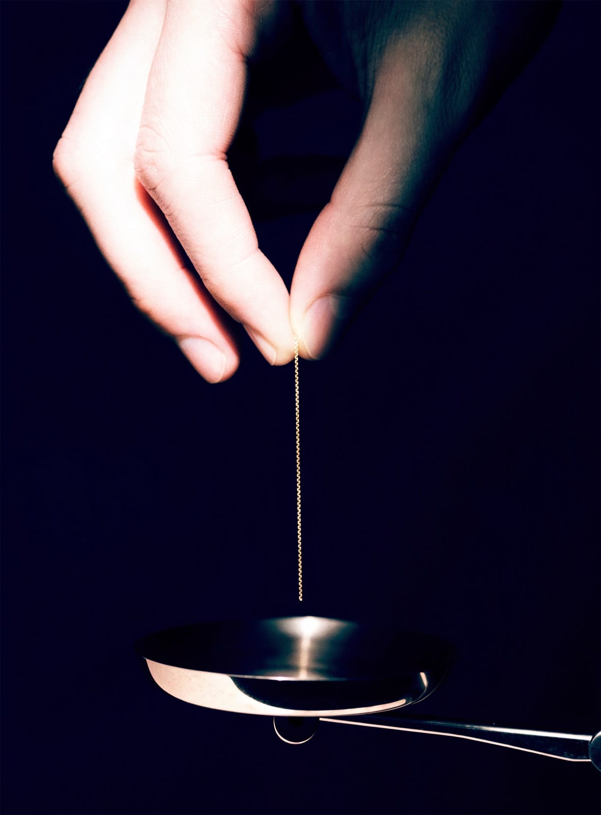 Eine Hand lässt eine feine Goldkette auf die Schale einer Feinwaage herab.