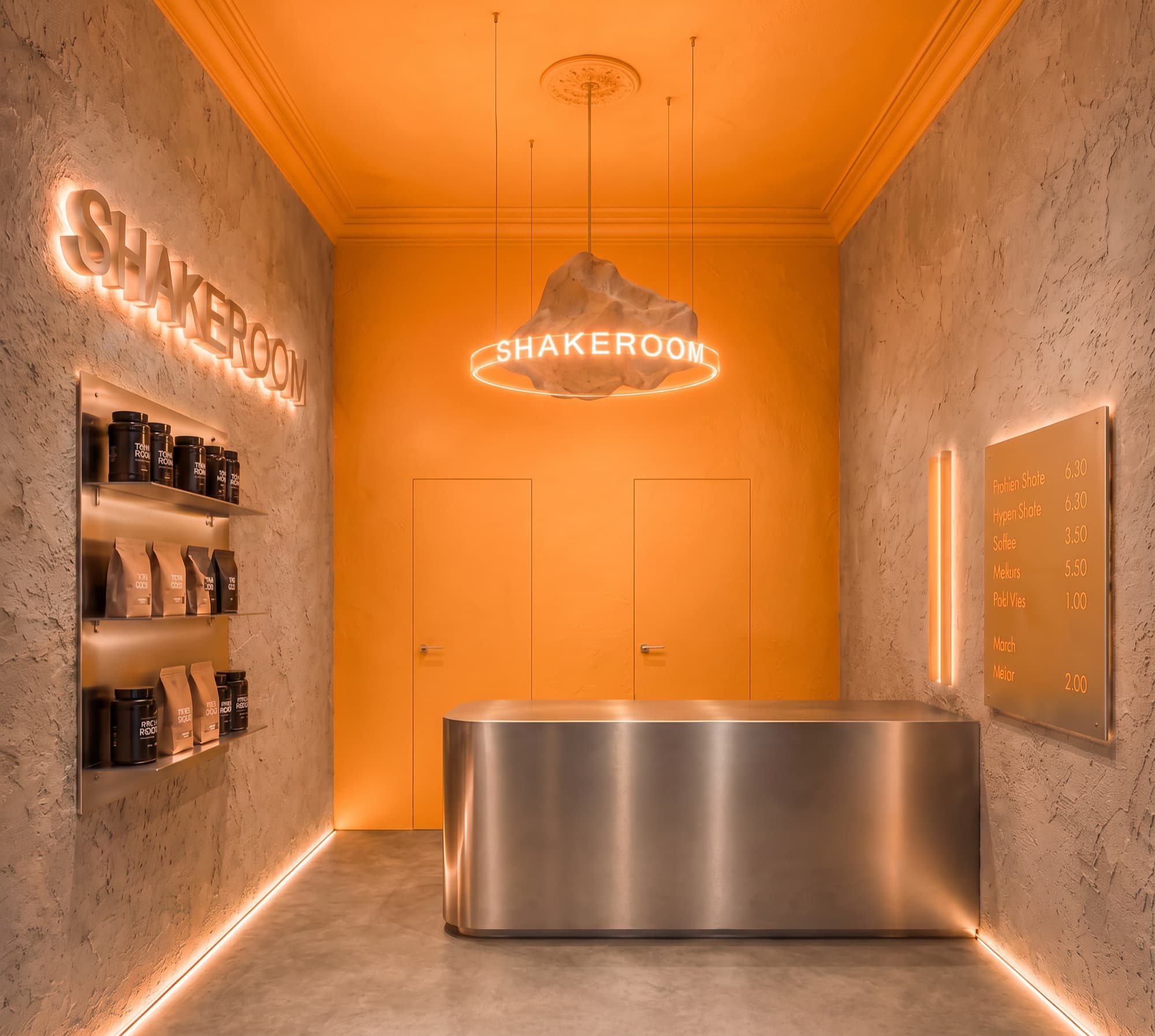 The Shakeroom interior: concrete walls, a steel counter and an orange back wall under a neon sign
